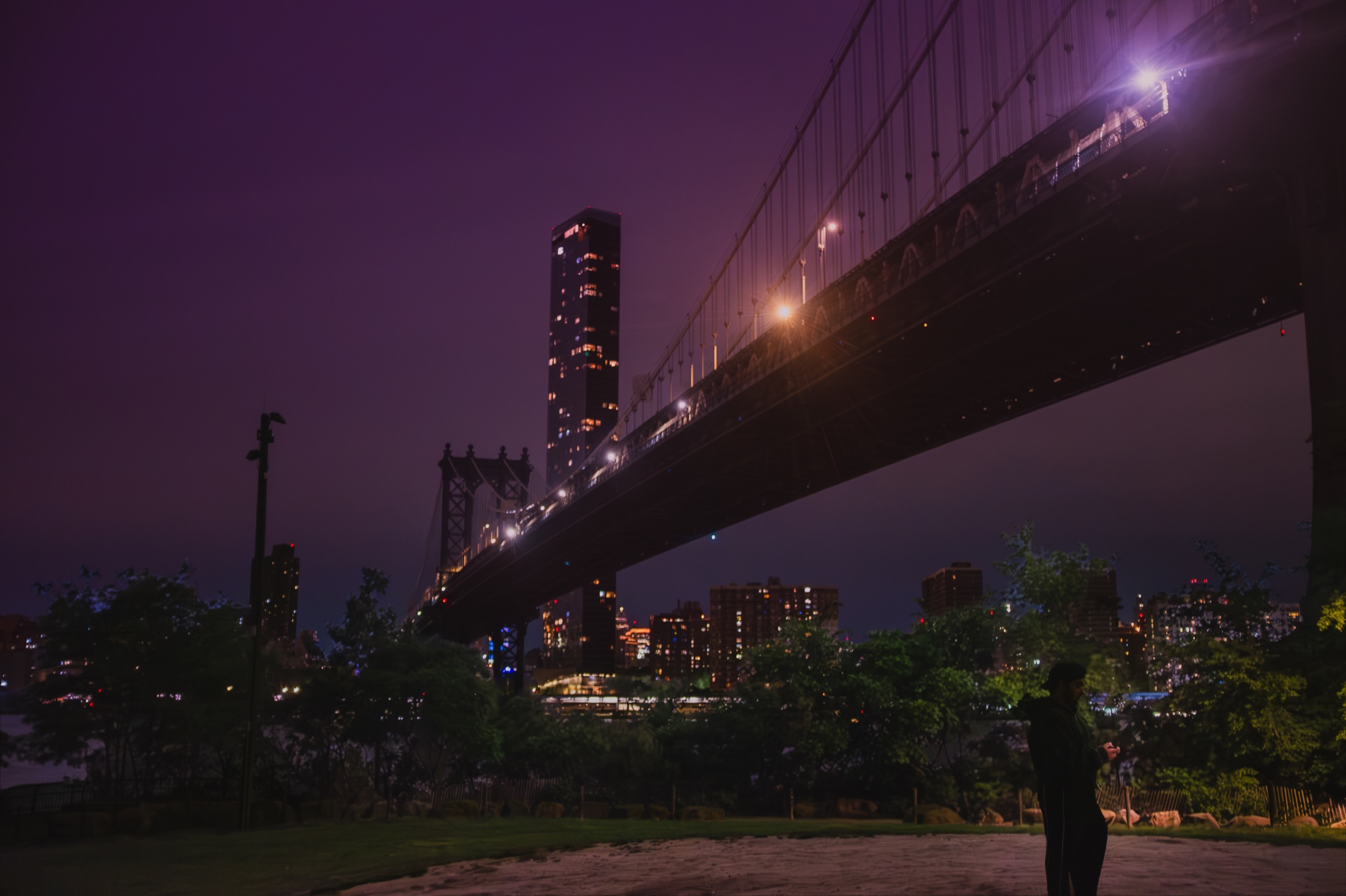 Manhattan Bridge crossing a purple night sky above a park
